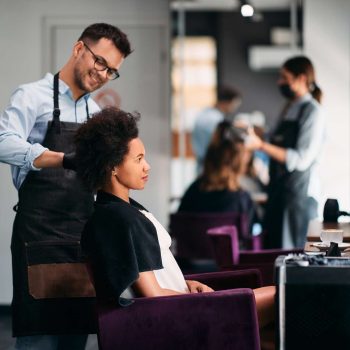 African American woman getting her hair styled by hairdresser at the salon.