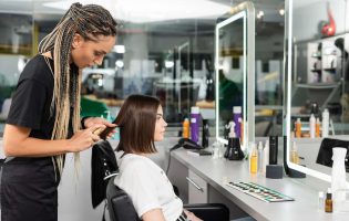 beauty salon work, professional salon worker with braids applying oil on hair of female client,