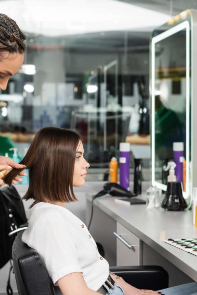 beauty salon work, professional salon worker with braids applying oil on hair of female client,