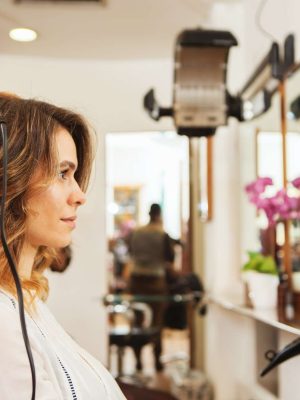 Hairdresser using curling tongs on customer's long brown hair in salon